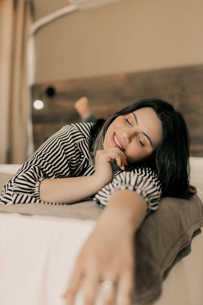 Smiling woman in striped shirt relaxing on a cozy bed indoors, exuding a warm and calm ambience.