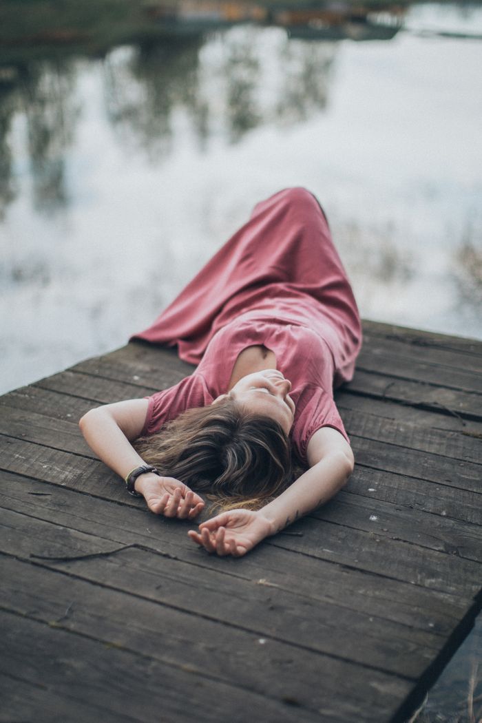 Woman in a pink dress lying on a wooden dock by the water, enjoying a calm moment outdoors.