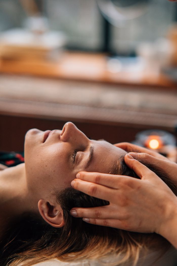 Woman enjoying a relaxing face massage indoors, eyes closed, with hands gently massaging temples.